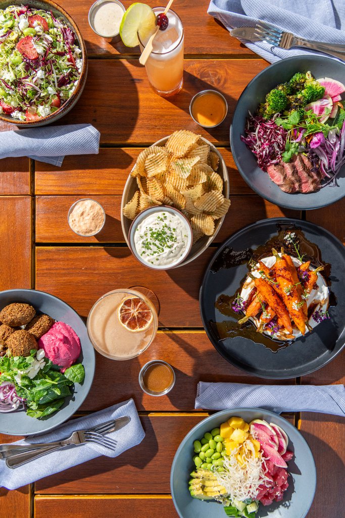 Aerial view of brussel salad, steak bowl, potato chips, meditterean bowl and poke bowl on sunny patio