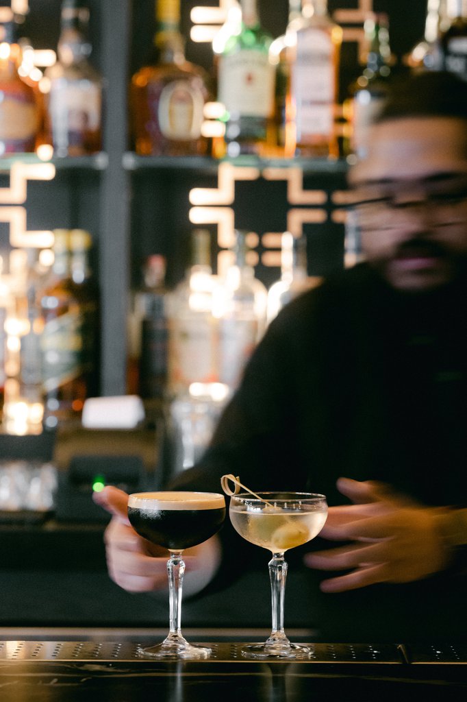 a bartender standing behind a well stocked bar serving two martinis at fora chicago the emily hotel fulton market west loop